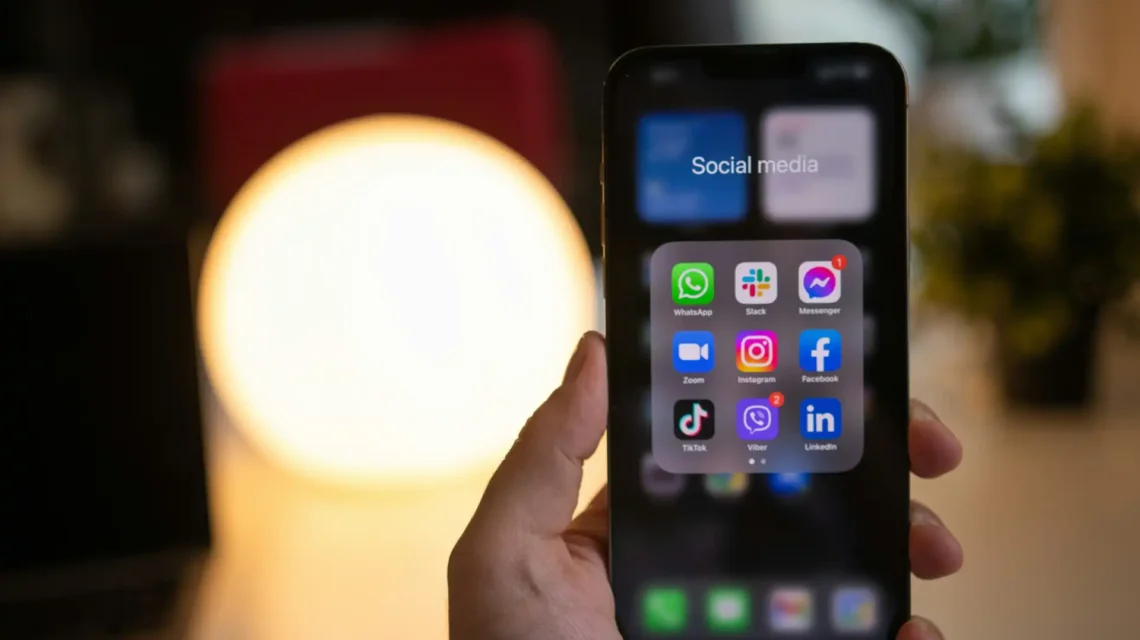 Pessoa segurando um smartphone com aplicativos de redes sociais na tela, ilustrando estratégias para incentivar clientes a criar conteúdo sobre sua marca.