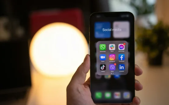 Pessoa segurando um smartphone com aplicativos de redes sociais na tela, ilustrando estratégias para incentivar clientes a criar conteúdo sobre sua marca.