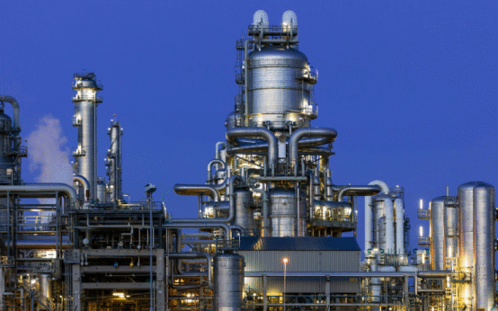 Complexo industrial com grandes torres metálicas, tubulações interligadas e iluminação artificial ao entardecer.