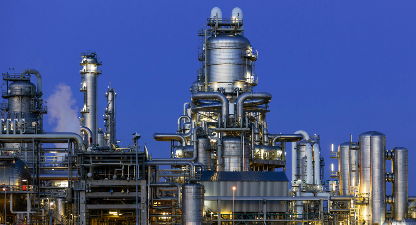 Complexo industrial com grandes torres metálicas, tubulações interligadas e iluminação artificial ao entardecer.
