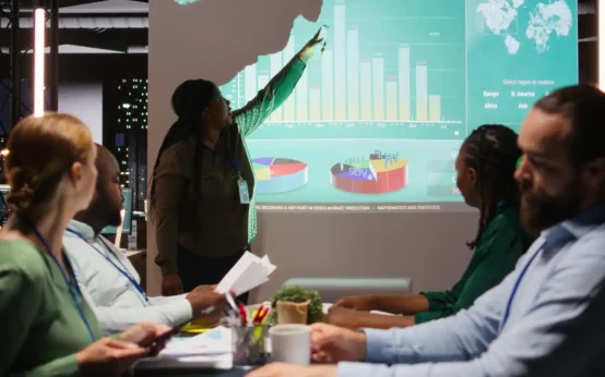 Equipe de analistas econômicos em reunião apresentando gráficos e tendências de mercado para prever futuro do mercado usando análise econômica.