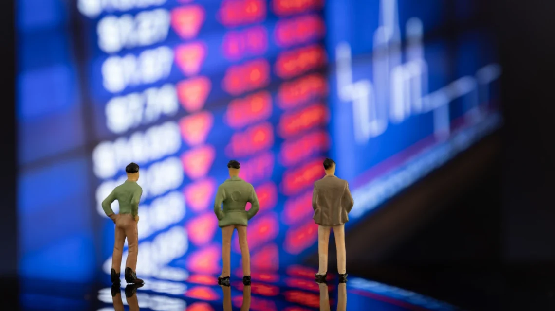 Três figuras de miniatura observando uma tela de mercado financeiro com ações em queda e gráficos, simbolizando estratégias empresariais em cenários de crise econômica.